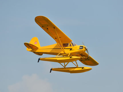 Yellow Phoenix Model PIPER J3 CUB  airplane with pontoons flying against a clear blue sky