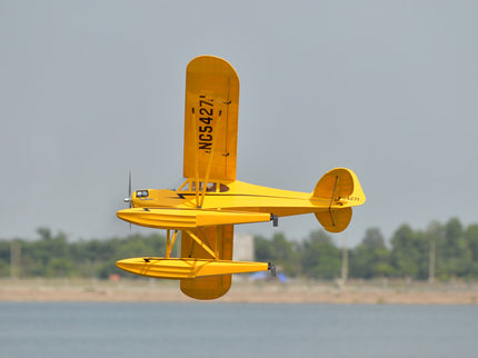 Yellow Phoenix Model PIPER J3 CUB  flying over a body of water with trees in the background