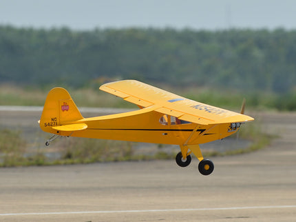 Yellow Phoenix Model PIPER J3 CUB airplane on a runway with a blurred background of trees